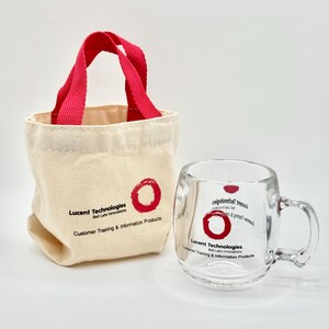 May include: A small beige canvas tote bag with red handles and a clear glass mug. Both items feature a red circle logo and the text Lucent Technologies Bell Labs Innovations Customer Training & Information Products printed in black ink.