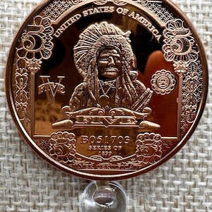 May include: A copper-colored coin featuring a portrait of a Native American in a headdress. The coin is inscribed with "UNITED STATES OF AMERICA" and "FIVE". The serial number "B051703" and "SERIES OF 1899" are also visible.