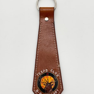 May include: Brown leather keychain with a circular emblem featuring a deer with antlers, a clock face, and the text "Texas Elks B.P.O.E 1981".