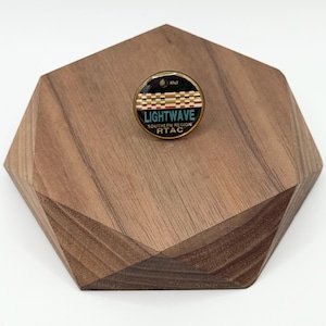 May include: A round pin with the text "LIGHTWAVE Southern Region RTAC" in white and blue, with a black and gold border. The pin is on a geometric wooden display. The pin also has the AT&T logo.