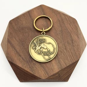 May include: A gold-colored metal keychain featuring a circular pendant with a map of Texas and the text "Austin 2012." The pendant also includes an image of a deer and the word "Elks." The keychain has a gold ring attached.