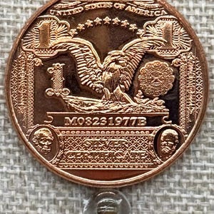 May include: A copper-colored coin with an eagle design, the text "UNITED STATES OF AMERICA", and the number "1". The coin also features the text "SILVER CERTIFICATE" and the date "M03231977B".