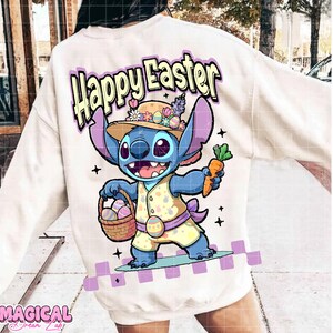 Puede incluir: Sudadera color crema con un personaje de dibujos animados sosteniendo una cesta de huevos de Pascua y una zanahoria. El personaje lleva un atuendo amarillo y un sombrero de paja. Las palabras "Happy Easter" están impresas encima del personaje en morado y amarillo.