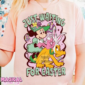 Puede incluir: Camiseta rosa con un gr&aacute;fico de estilo vintage de Mickey Mouse vestido de conejito de Pascua, montando a Pluto. El texto "Just Waiting for Easter" est&aacute; impreso en la camiseta.