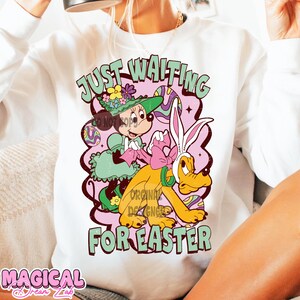 Puede incluir: Sudadera blanca con un estampado gr&aacute;fico de Mickey Mouse y Pluto vestidos con atuendos de Pascua. El texto "Just Waiting For Easter" est&aacute; impreso en la sudadera.