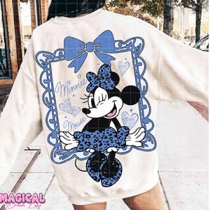 May include: Cream-colored sweatshirt featuring a Minnie Mouse graphic. The design includes a blue bow, a framed image of Minnie, and the words "Minnie Mouse." The graphic has a distressed, vintage look.
