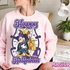 May include: A light pink sweatshirt with a Halloween-themed graphic. The graphic features a cartoon character dressed as a witch with the words "Happy Halloween" in purple script. A witch hat and broom are also included.