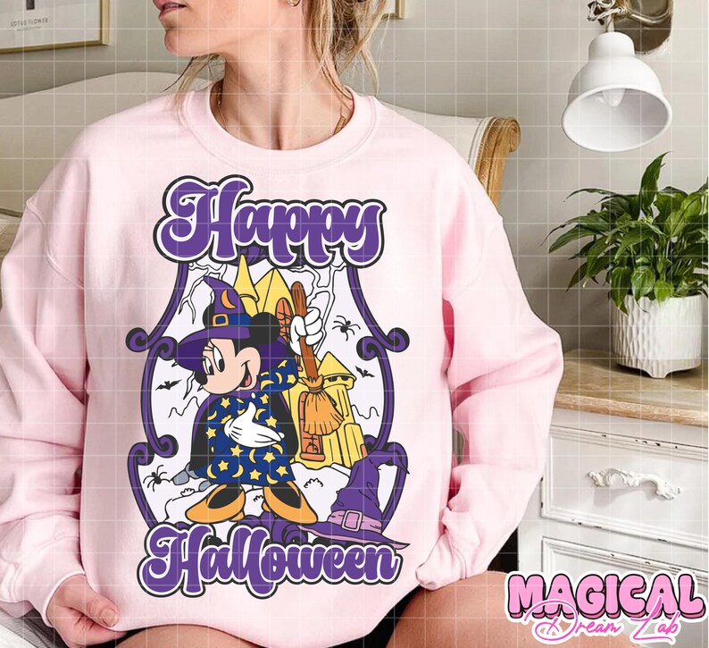 May include: A light pink sweatshirt with a Halloween-themed graphic. The graphic features a cartoon character dressed as a witch with the words "Happy Halloween" in purple script. A witch hat and broom are also included.