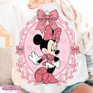 May include: A white sweatshirt featuring a pink Minnie Mouse graphic. The graphic includes Minnie Mouse in a pink polka-dot dress and bow, set within a pink oval frame with hearts and bows. The words "MAGICAL DREAM LAB" are at the bottom.