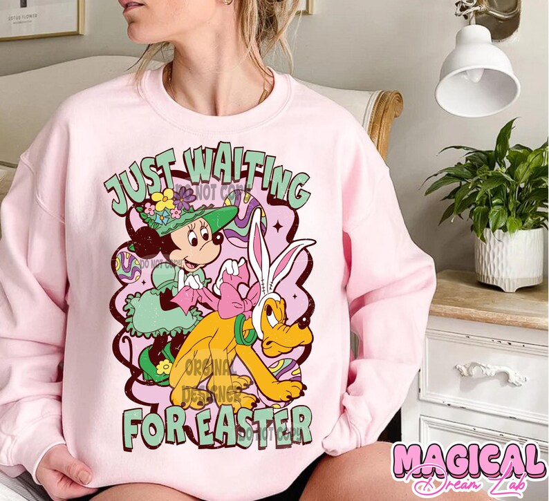 Puede incluir: Sudadera rosa con un gr&aacute;fico de Mickey Mouse y Pluto en un dise&ntilde;o de Pascua. El texto "Just Waiting for Easter" est&aacute; impreso en la sudadera.