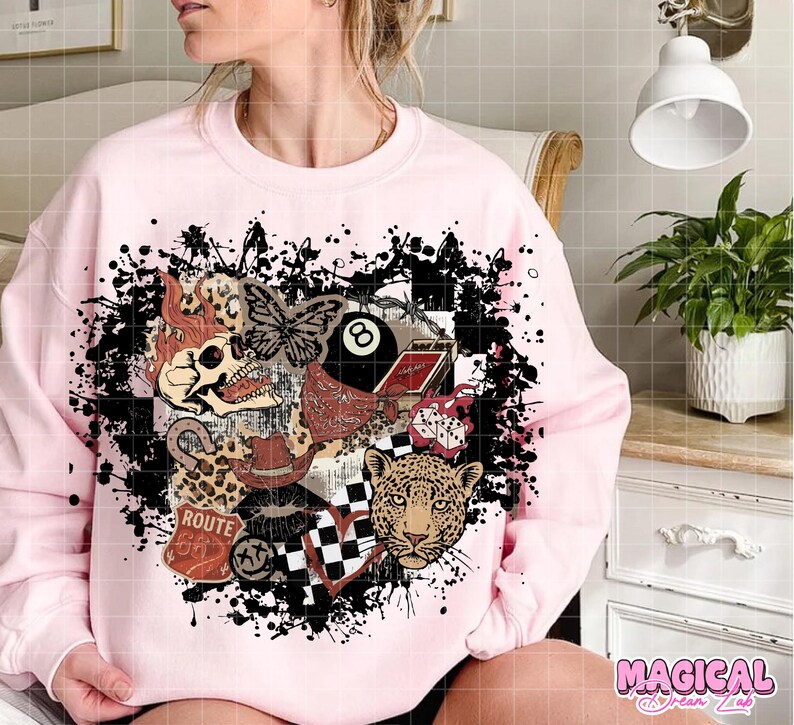 May include: Light pink sweatshirt with a graphic design featuring a skull, butterfly, leopard, Route 66 sign, and an 8-ball. The design is surrounded by black paint splatters. The text "MAGICAL Dream Lab" is in the bottom right corner.