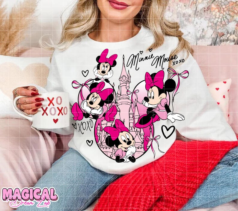 May include: White long-sleeved sweatshirt featuring a Minnie Mouse design in pink and black. The design includes Minnie Mouse characters, hearts, and the text "Minnie Mouse XOXO". A white mug with "XO XOXO" is held in the hand.