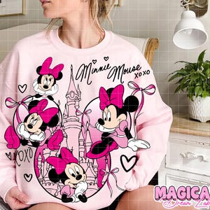 May include: A light pink sweatshirt featuring Minnie Mouse in a circular design with a castle and hearts. The words "Minnie Mouse xoxo" are written in cursive. The sweatshirt has a cartoon graphic of Minnie Mouse in pink.