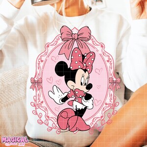 May include: White sweatshirt featuring a pink Minnie Mouse graphic. The graphic includes a pink bow with white polka dots, a pink frame, and pink bows. The words "MAGICAL DREAM LAB" are at the bottom left.