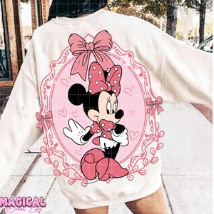May include: A white sweatshirt featuring a pink Minnie Mouse graphic. The graphic includes a polka-dot bow, hearts, and the text "Magical @ Dream Lab". The design is set within a pink oval frame.