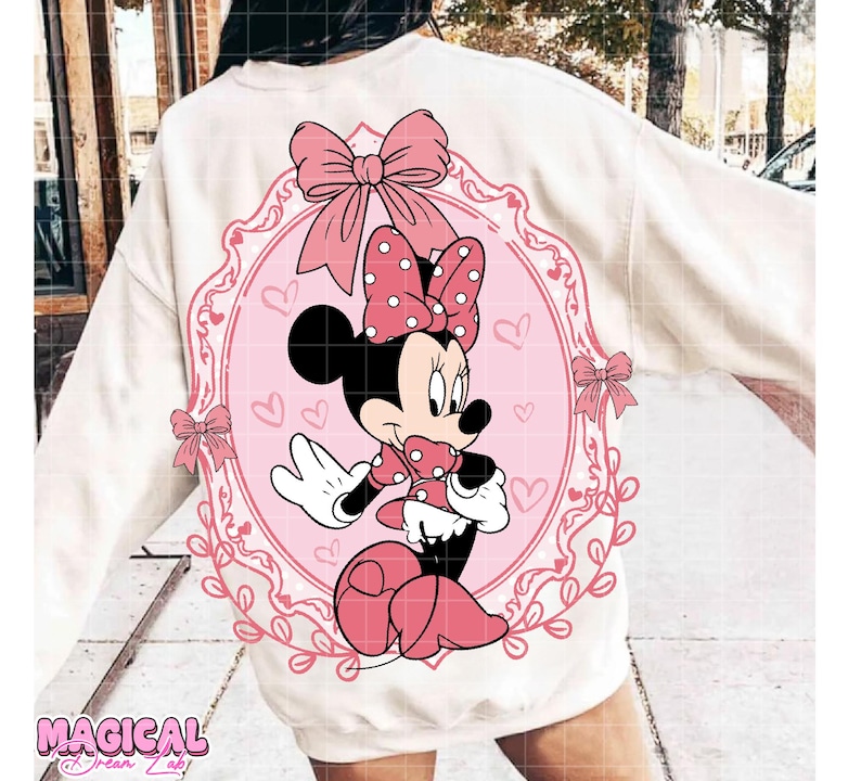 May include: A white sweatshirt featuring a pink Minnie Mouse graphic. The graphic includes a polka-dot bow, hearts, and the text "Magical @ Dream Lab". The design is set within a pink oval frame.