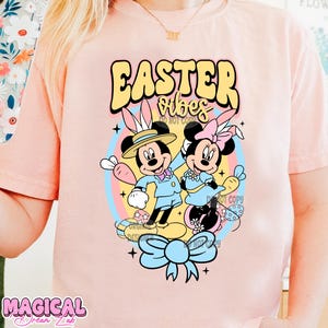 May include: Pink t-shirt with a graphic of Mickey Mouse and Minnie Mouse dressed in Easter outfits. The text "Easter Vibes" is above the characters.