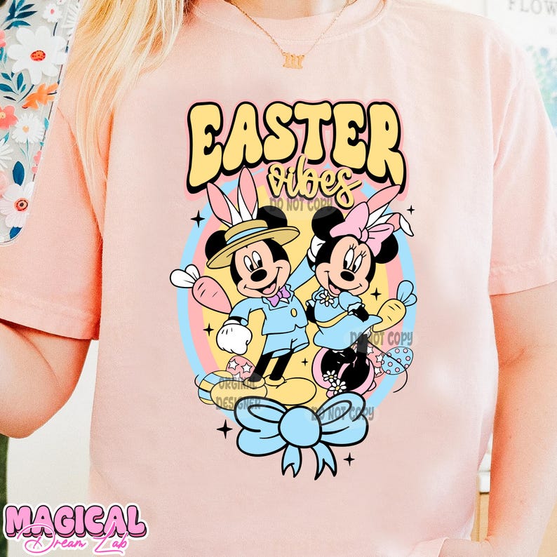 May include: Pink t-shirt with a graphic of Mickey Mouse and Minnie Mouse dressed in Easter outfits. The text "Easter Vibes" is above the characters.