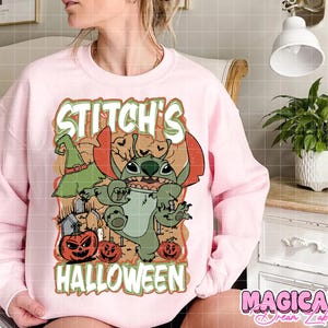 May include: Pink sweatshirt featuring a Halloween-themed graphic of Stitch, a green alien character, with a witch hat, pumpkins, and the text "Stitch's Halloween". The design is in orange, green, and brown.