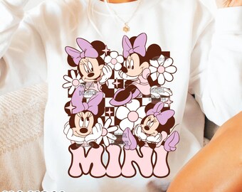 May include: White sweatshirt with a graphic of four cartoon mice wearing pink bows and surrounded by pink flowers. The text "MINI" is printed in pink and brown letters.