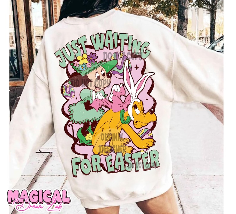 Puede incluir: Sudadera blanca con un gr&aacute;fico de dibujos animados de Mickey Mouse y Pluto vestidos con atuendos de Pascua. El texto "Just Waiting For Easter" est&aacute; impreso en la sudadera.
