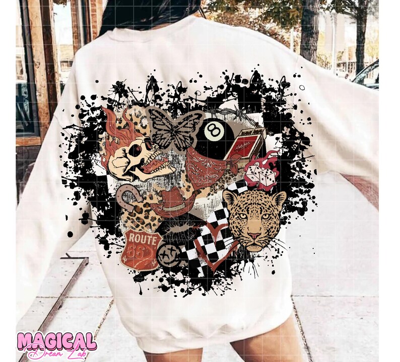 May include: Cream-colored sweatshirt with a graphic design featuring a skull, butterfly, leopard, and other vintage-style elements. The design includes a Route 66 sign, an 8-ball, and a checkered heart, all set against a black splatter background.