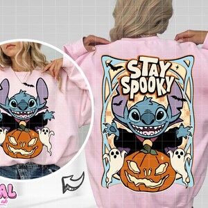 May include: Pink sweatshirt featuring a cartoon character with a pumpkin and ghosts. The design includes the text "Stay Spooky" and bats. The sweatshirt has long sleeves and a crew neck.