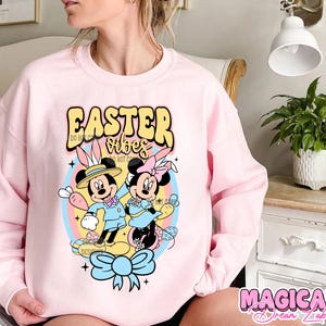 May include: Pink sweatshirt with a graphic of Mickey Mouse and Minnie Mouse dressed in Easter outfits. The text "Easter Vibes" is printed on the sweatshirt.