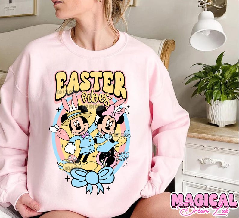 May include: Pink sweatshirt with a graphic of Mickey Mouse and Minnie Mouse dressed in Easter outfits. The text "Easter Vibes" is printed on the sweatshirt.