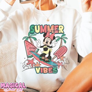 May include: White sweatshirt with a colorful graphic print of a cartoon mouse riding a surfboard with the text "Summer Vibes".