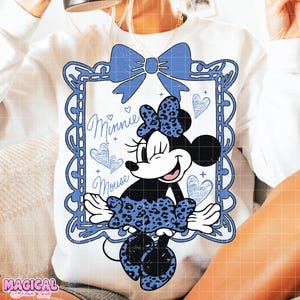 May include: White sweatshirt featuring a blue framed Minnie Mouse graphic. The Minnie Mouse design includes a blue bow, a leopard print dress, and the words "Minnie Mouse". The design also includes blue hearts.