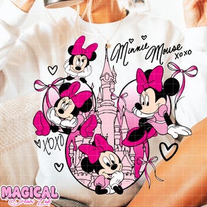 May include: White sweatshirt featuring a Minnie Mouse graphic in pink and black. The design includes Minnie Mouse characters, a castle, hearts, and the text "Minnie Mouse XOXO". The bottom left corner has the text "MAGICAL DREAM LAB".