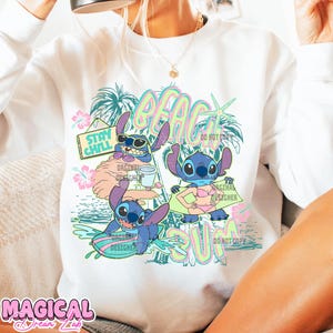May include: White sweatshirt featuring a colorful graphic of the character Stitch at the beach. The design includes the words "BEACH SUN" and "STAY CHILL", along with tropical elements like palm trees and flowers. The words "ORIGINAL DESIGNER" are also visible.