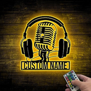 Puede incluir: Una pieza de arte mural iluminada en negro y amarillo con un diseño de micrófono y auriculares. Las palabras "CUSTOM NAME" se muestran en una base rectangular. Un mando a distancia es visible en la esquina inferior derecha.