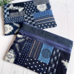 以下が含まれることがあります： 青と白の色合いのパッチワークデザインの、2つの長方形のジッパー付きポーチ。 ポーチには、水玉模様、ストライプ、花柄など、さまざまなパターンがあります。 ジッパーは、お揃いの濃い青色です。
