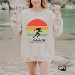 May include: A beige sweatshirt with a vintage-style graphic of a runner with the text "If I collapse please pause my watch".