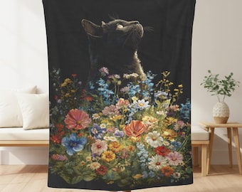 May include: A black cat blanket featuring a detailed illustration of a black cat looking upwards, surrounded by a vibrant array of colorful wildflowers. The blanket has a dark background, highlighting the cat and flowers.