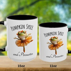 May include: Two white ceramic mugs with black interiors and handles. Each mug features a graphic of a green frog wearing an orange tutu, with the text PUMPKIN SPICE and and Pirouettes printed in black. The mugs are labeled 15oz and 11oz.
