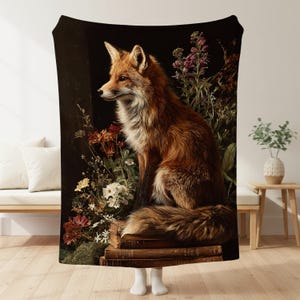 May include: A plush blanket featuring a detailed illustration of a fox with reddish-brown fur, sitting atop a stack of books. The fox is surrounded by flowers in shades of red, white, and purple against a dark background. The blanket is soft and cozy.