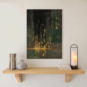 May include: Abstract art print with a dark green and black background, featuring gold accents that resemble city lights reflecting on water. The artwork hangs above a wooden shelf with books, a vase, and a decorative lamp.