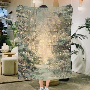 May include: A cozy blanket featuring a winter forest scene with snow-covered trees and a path leading into the light. The design includes soft, muted colors and twinkling lights, creating a warm and inviting atmosphere. This blanket is perfect for snuggling up during the colder months.
