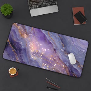 May include: A large rectangular desk mat with a purple and gold marble design. The mat has a black border and a white computer mouse is on the right side. A laptop, notebook, and coffee cup are also on the dark surface.