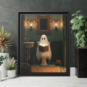 May include: A framed wall art print depicting a white ghost draped in a sheet sitting on a toilet in a dimly lit bathroom, reading an open book. The scene features dark wood paneling, two wall sconces with glowing candles, and a mirror.