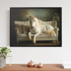 May include: A framed wall art print depicting a white horse resting on an ornate, cream-colored upholstered sofa with tufted detailing and decorative pillows. The scene is set against a dark, moody background with soft lighting and floral accents.