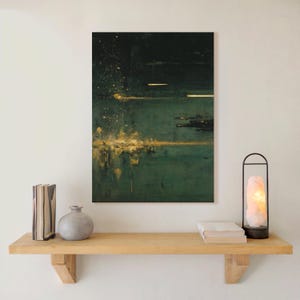 May include: Abstract art print with a dark green and gold color palette. The artwork features a textured appearance with splatters and horizontal lines of gold against a deep green background. The print is displayed above a wooden shelf.