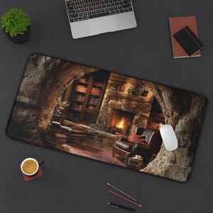 Puede incluir: Alfombrilla de escritorio rectangular con una acogedora escena de biblioteca con chimenea, sillón de cuero y estanterías. La alfombrilla tiene un borde negro y un ratón de ordenador está en el lado derecho. También se ve una taza de café y una pequeña planta.
