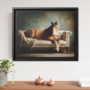 May include: A framed wall art print depicting a brown horse with a white blaze on its face, resting on a beige tufted sofa. The horse is positioned centrally, facing forward, with a textured blanket draped over the sofa seat and backrest.