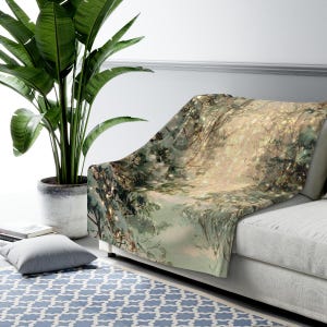 May include: A soft throw blanket draped over a sofa, featuring a nature-inspired design. The blanket showcases a forest scene with trees, branches, and a soft, glowing light. The color palette includes greens, browns, and beige tones.