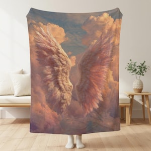 May include: A rectangular throw blanket featuring a printed image of large, detailed white feathered wings spread wide against a backdrop of soft, sunset-colored clouds in shades of pink, orange, and light blue, with a smooth, fabric texture.