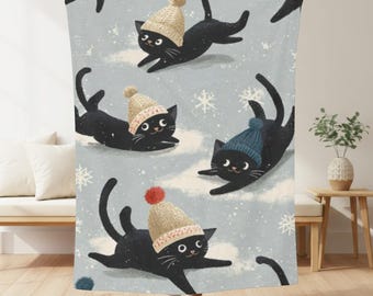 May include: A light blue blanket featuring a repeating pattern of black cats wearing winter hats and playing in the snow. The cats have smiling faces and are surrounded by snowflakes. The blanket is soft and cozy.